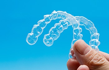 Hand holding two clear aligners against blue background