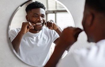 Man smiling while flossing teeth at restaurant
