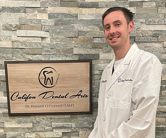 Califon New Jersey dentist Doctor Russell O Connell next to wooden sign for Califon Dental Arts